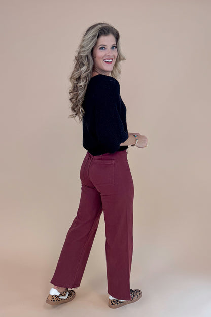 Woman wearing a black top and maroon pants against a beige background
