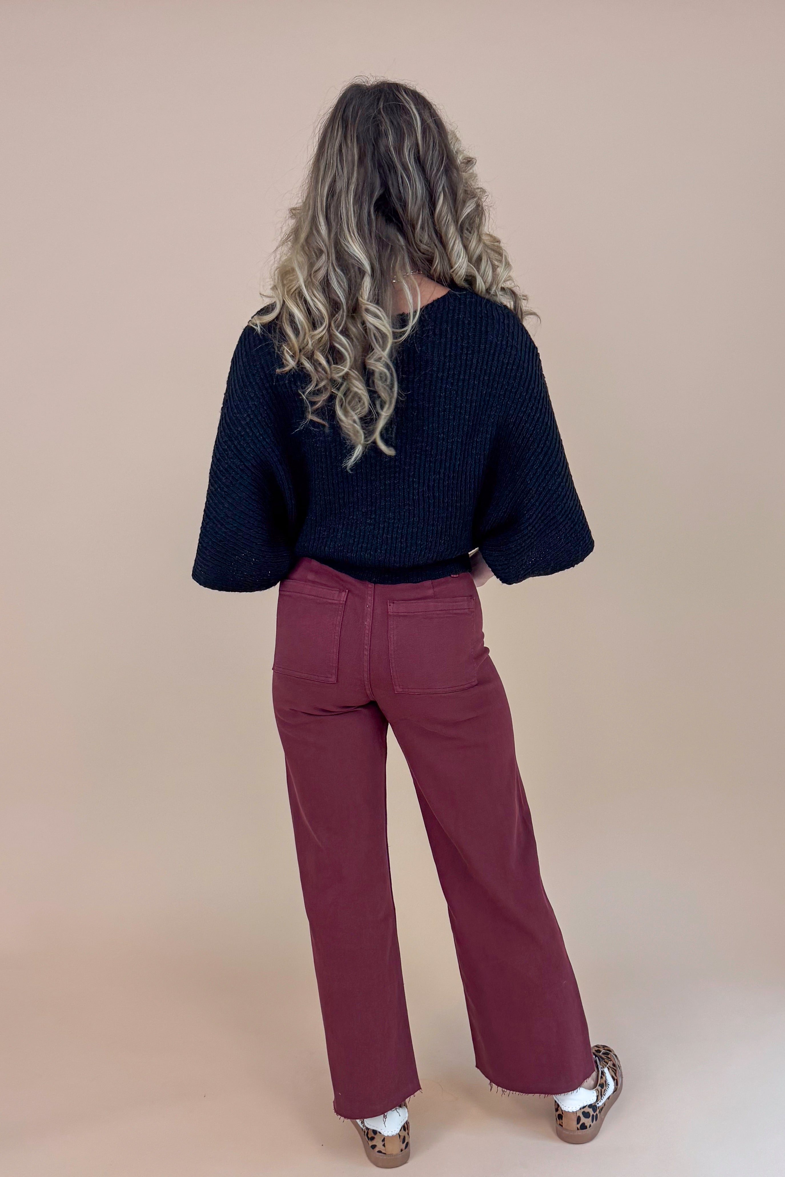 Person wearing a black top and maroon pants against a beige background