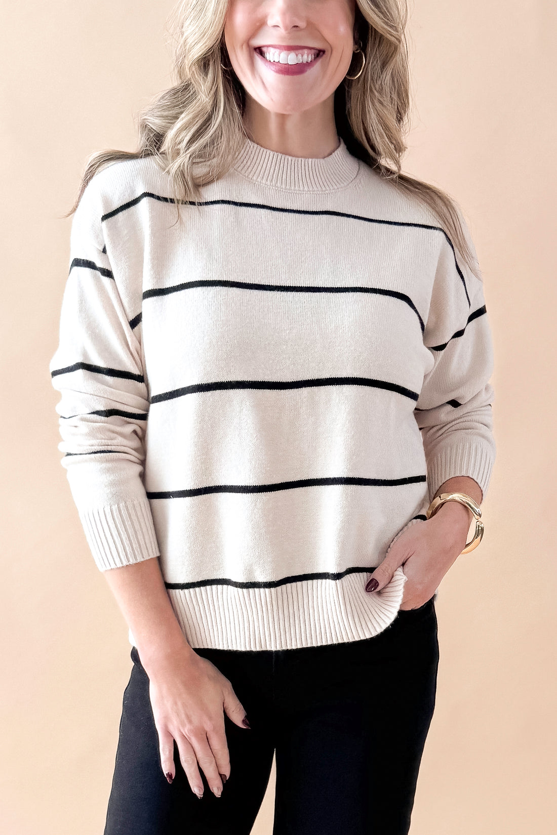 Front detailed view of woman wearing striped sweater with jeans against tan studio background.
