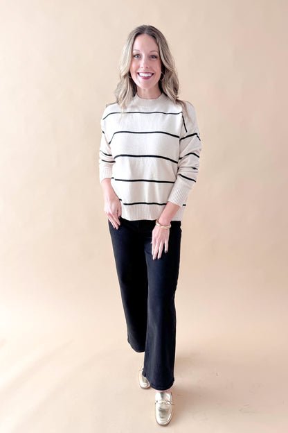 Front view of woman wearing striped sweater with jeans against tan studio background.