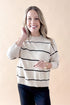 Front view of woman wearing striped sweater with jeans against tan studio background.