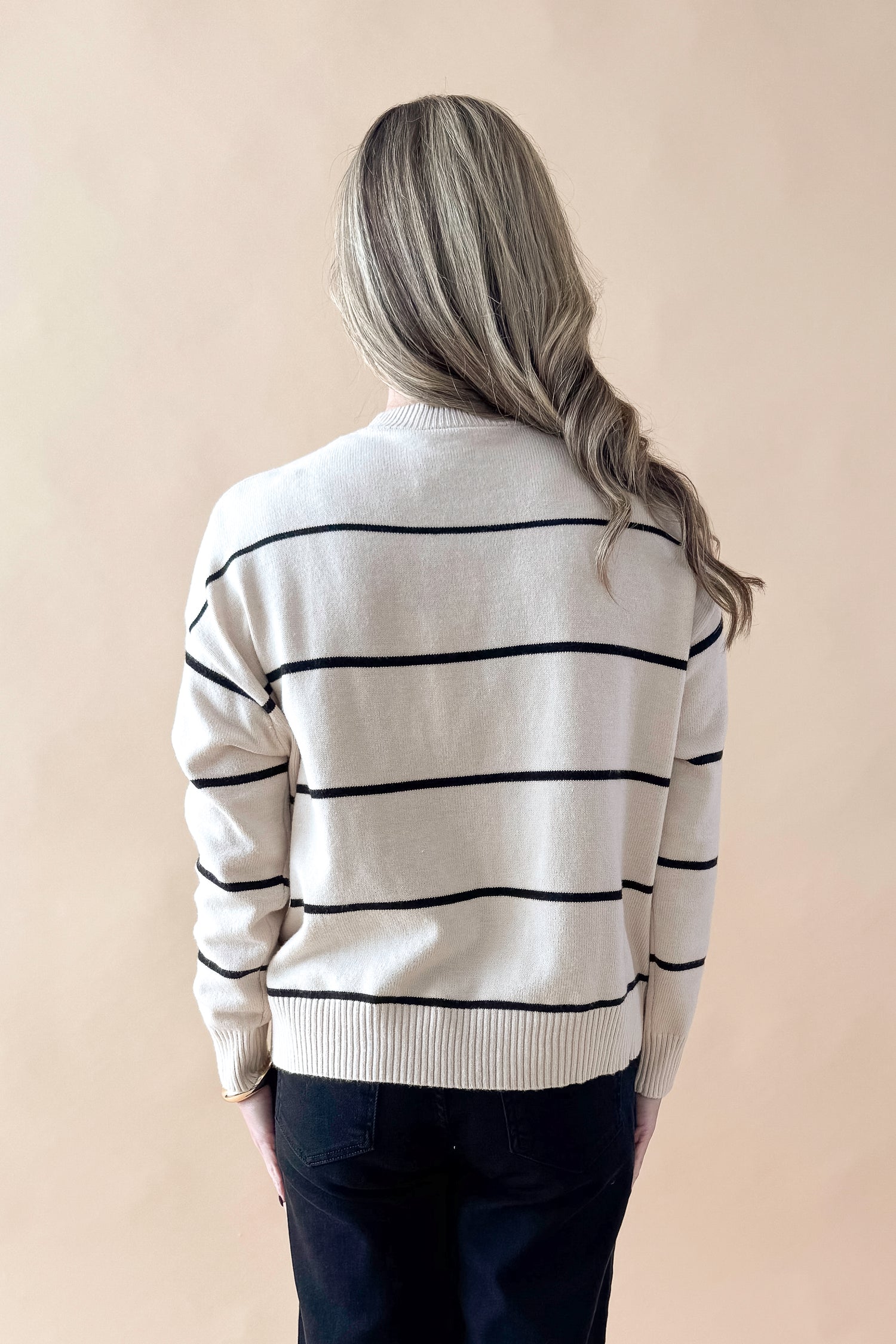Back view of woman wearing striped sweater with jeans against tan studio background.