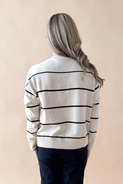 Back view of woman wearing striped sweater with jeans against tan studio background.