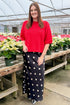 Woman in a red top and polka dot skirt standing by poinsettias.