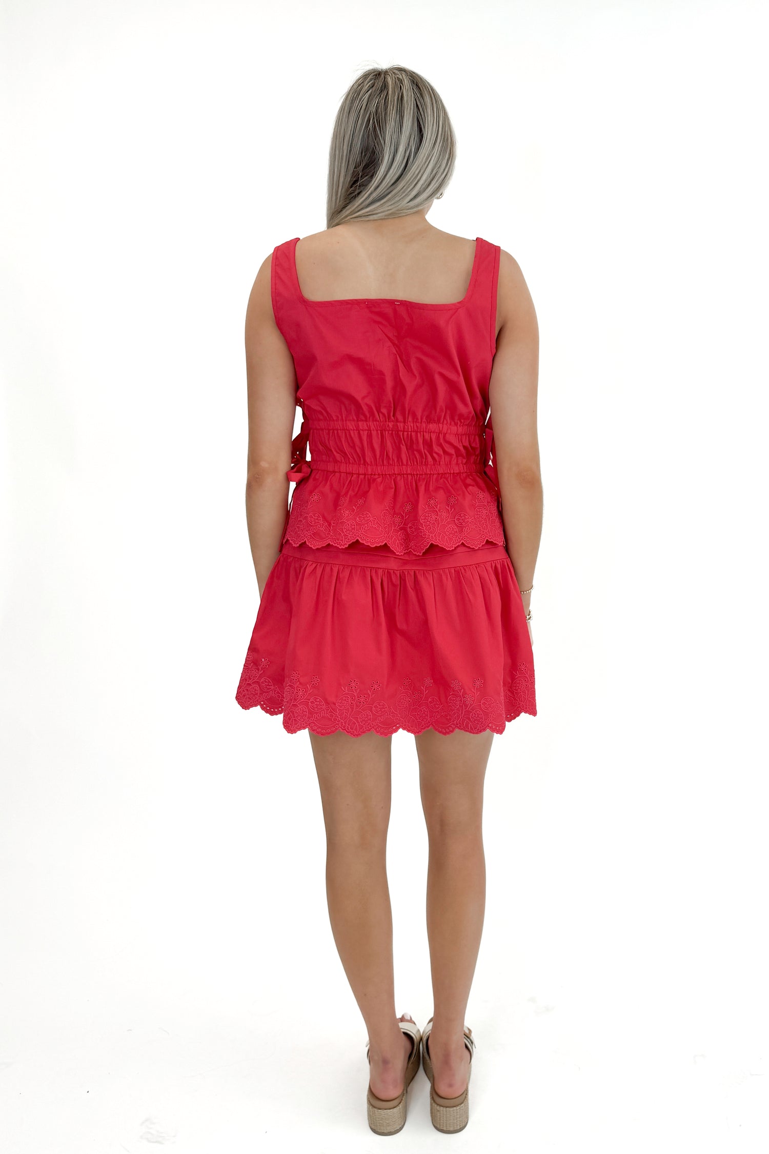 Back view of woman wearing Red Eyelet Hem Tie Detail Tank with matching skirt against white studio background.