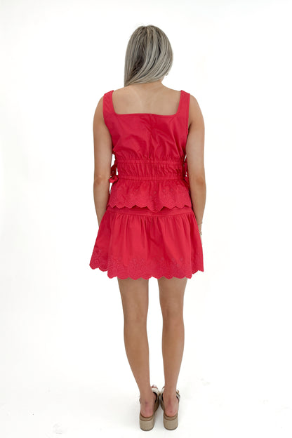 Back view of woman wearing Red Eyelet Hem Tie Detail Tank with matching skirt against white studio background.