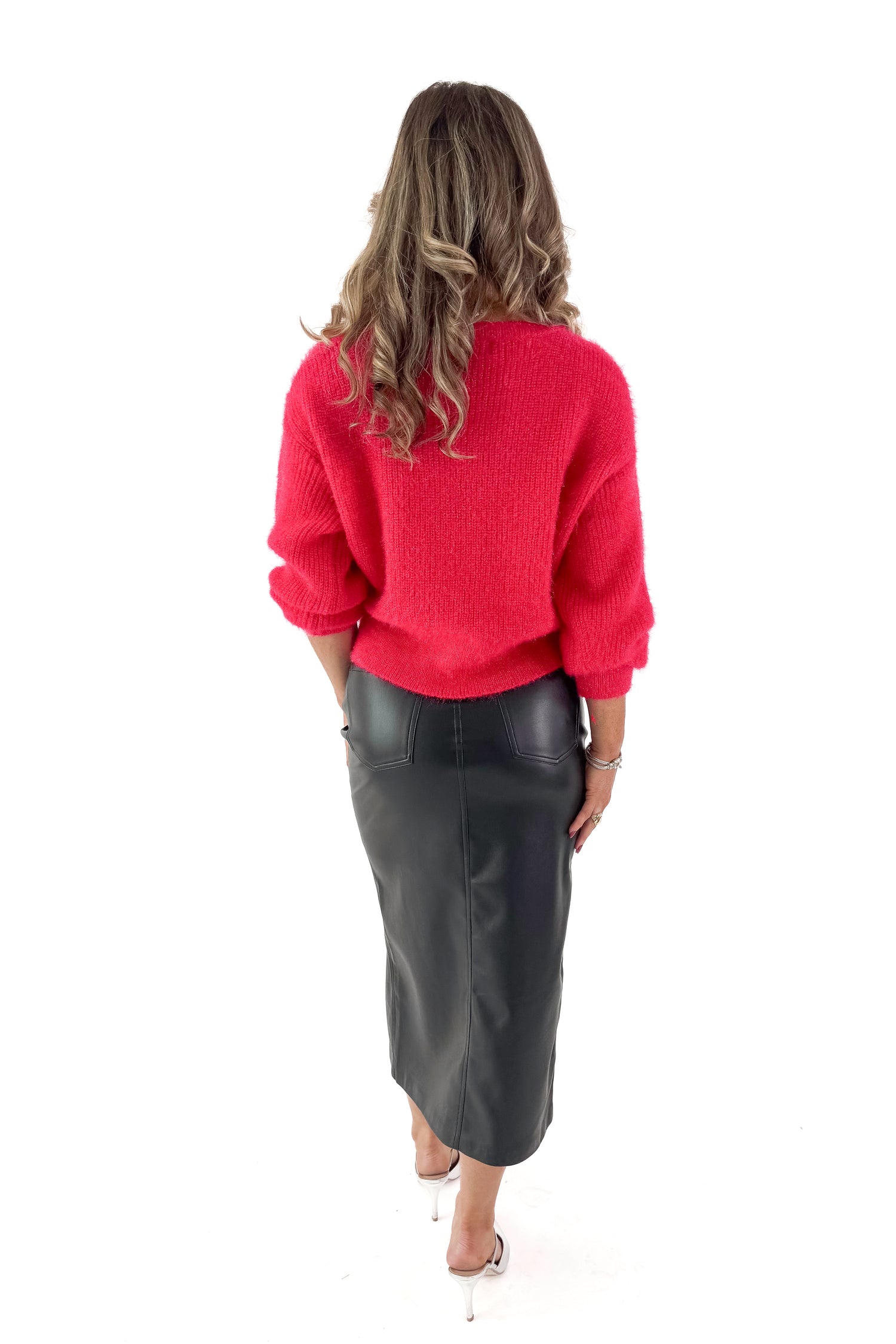 Back view of woman wearing black faux leather skirt with red top against white studio background.