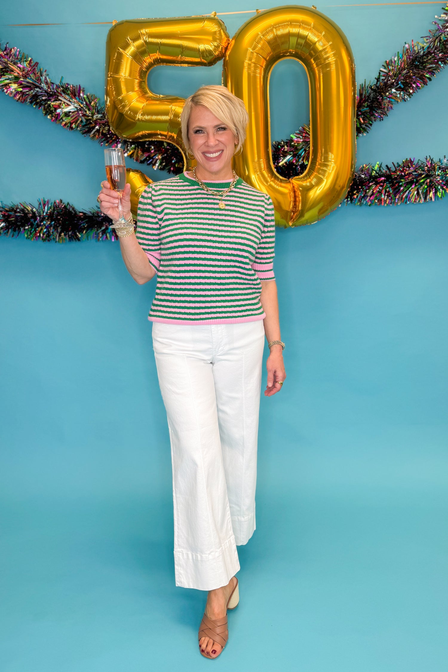 Front view of woman wearing Green &amp; Pink Striped Short Sleeve Sweater with jeans against blue background.