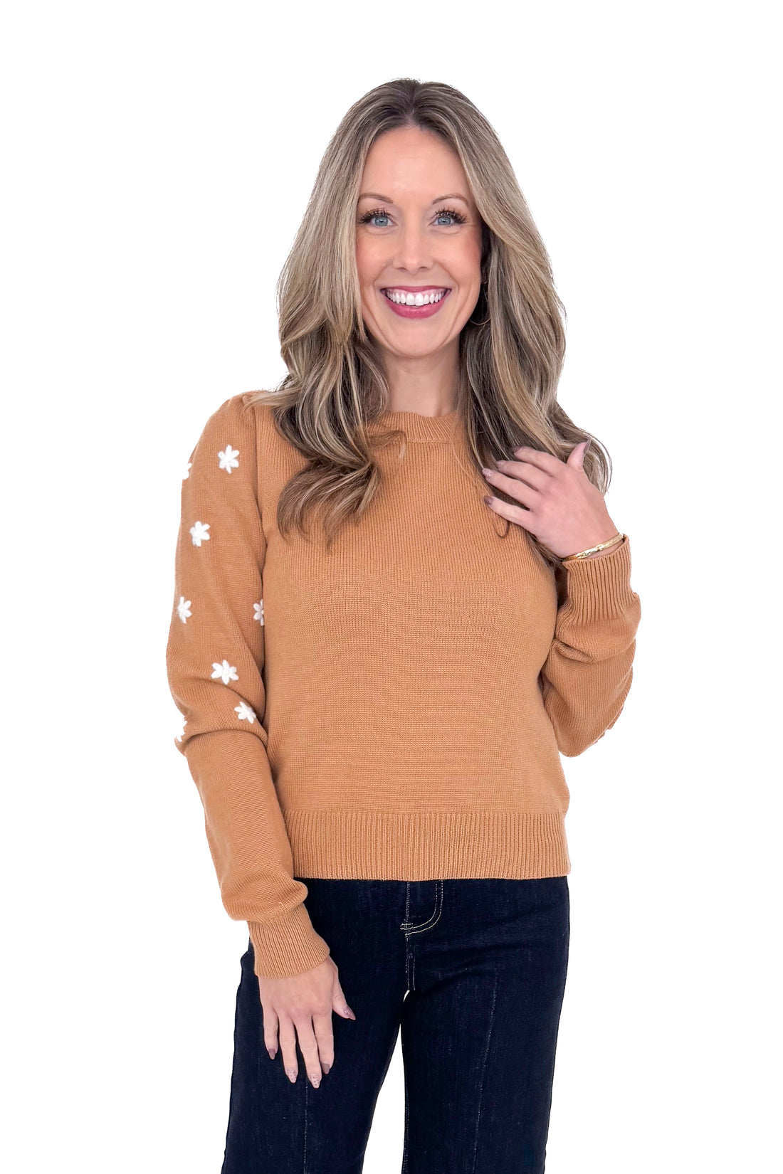 Woman in studio wearing Taupe With Embroidered Floral Sleeve Sweater and blue jeans with white background.