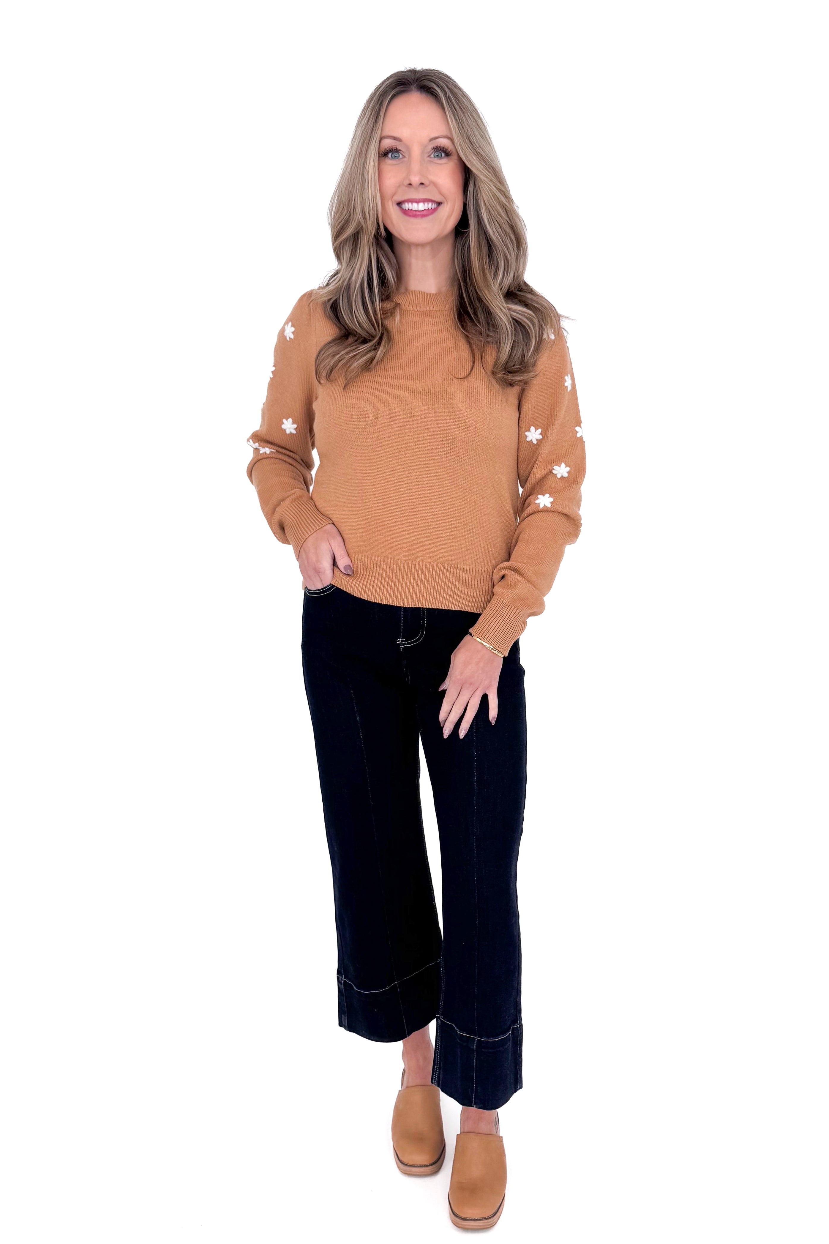 Woman in studio wearing Taupe With Embroidered Floral Sleeve Sweater and blue jeans with white background. 