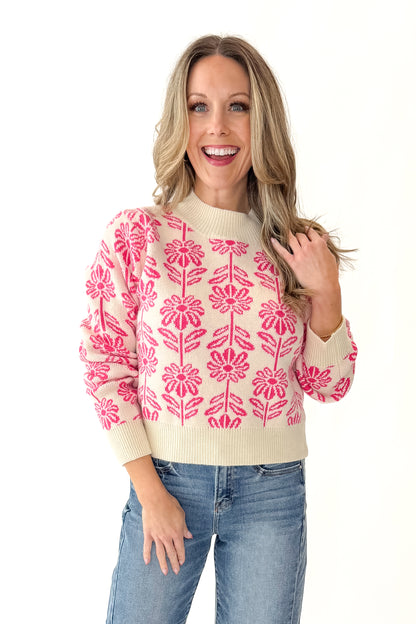 Front view of woman wearing Cream and Pink Floral Patterned Sweater with jeans against white studio background. 