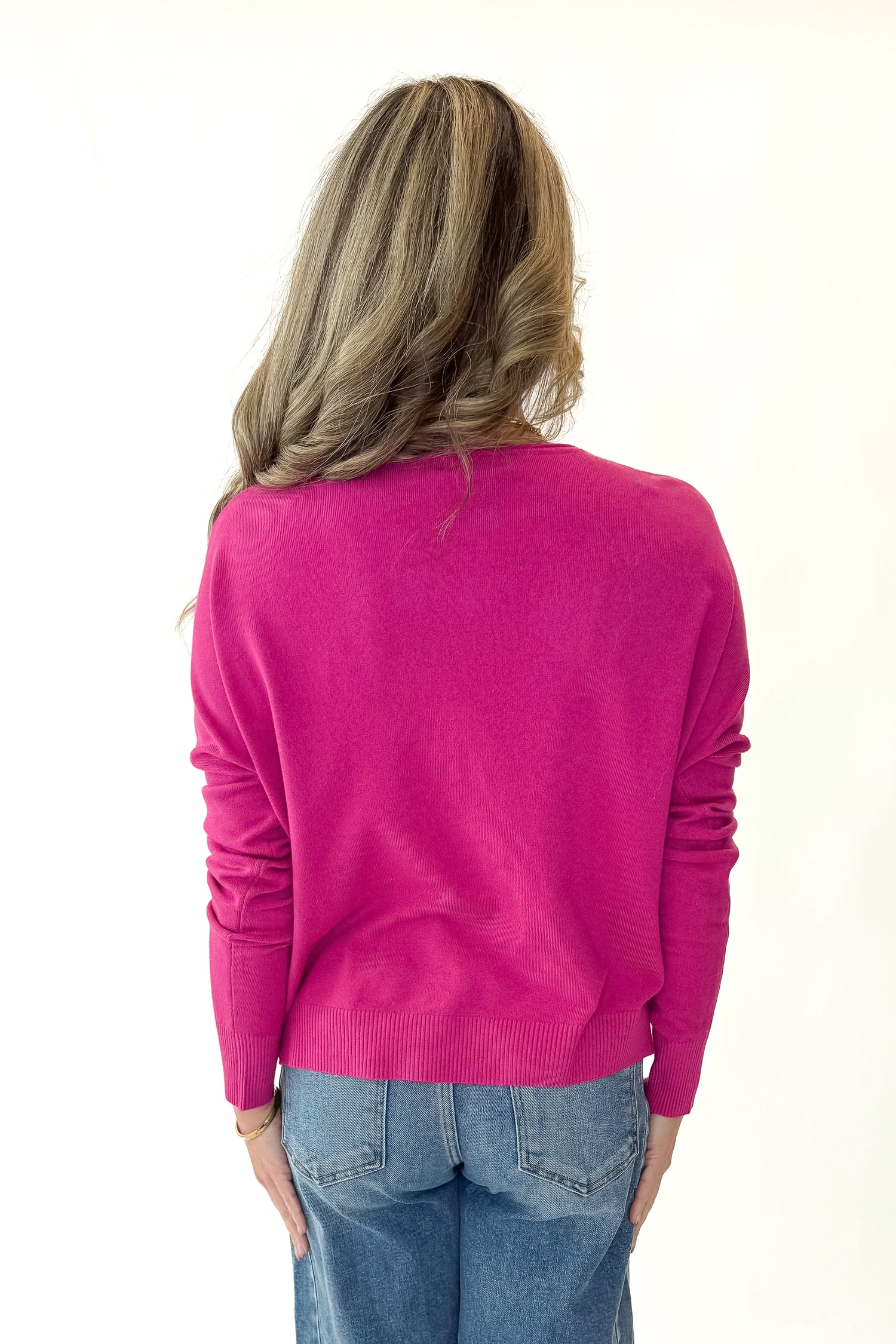Back view of woman wearing Magenta Center Seam Sweater with jeans against white studio background.