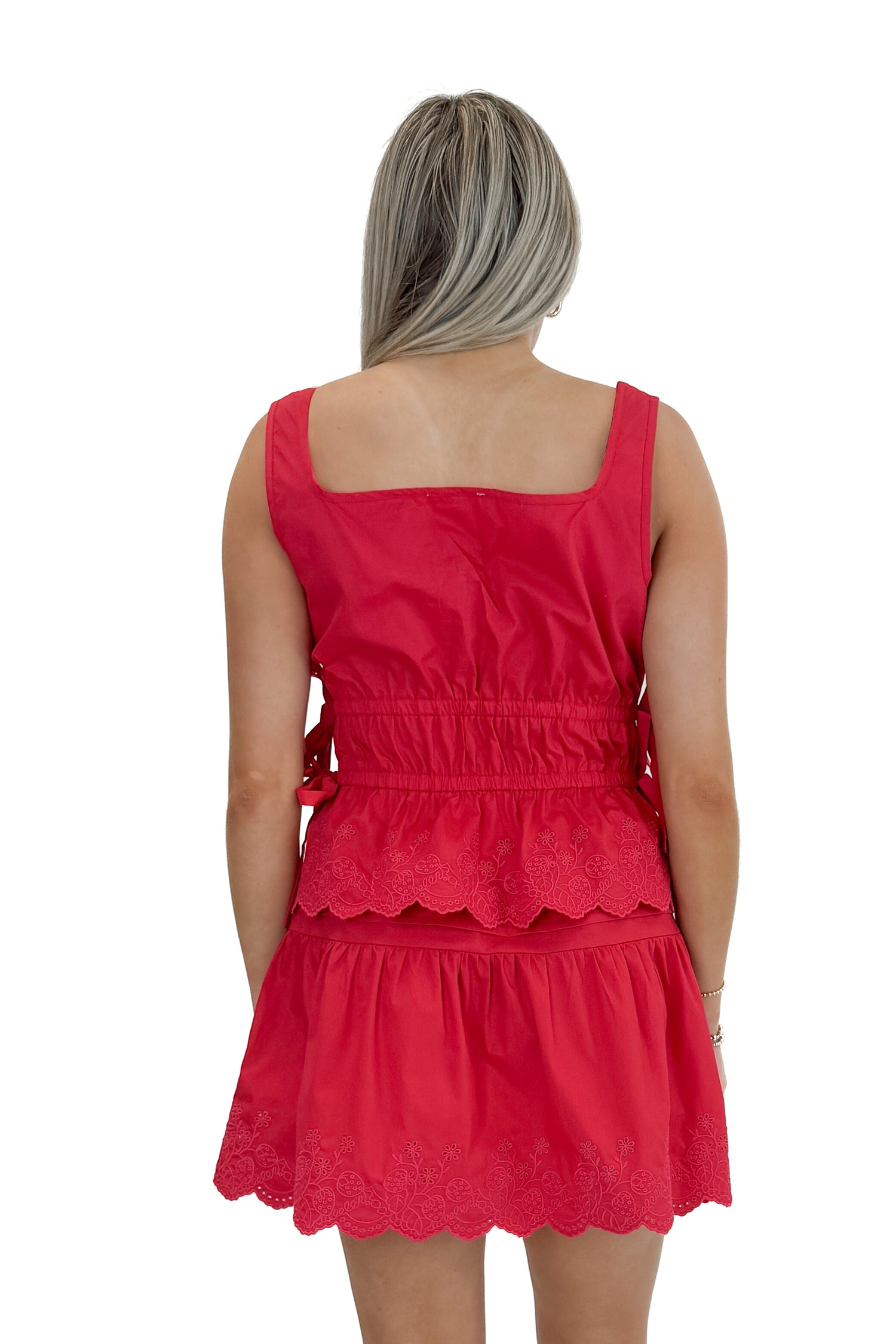 Back view of woman wearing Red Eyelet Hem Tie Detail Tank with matching skirt against white studio background.