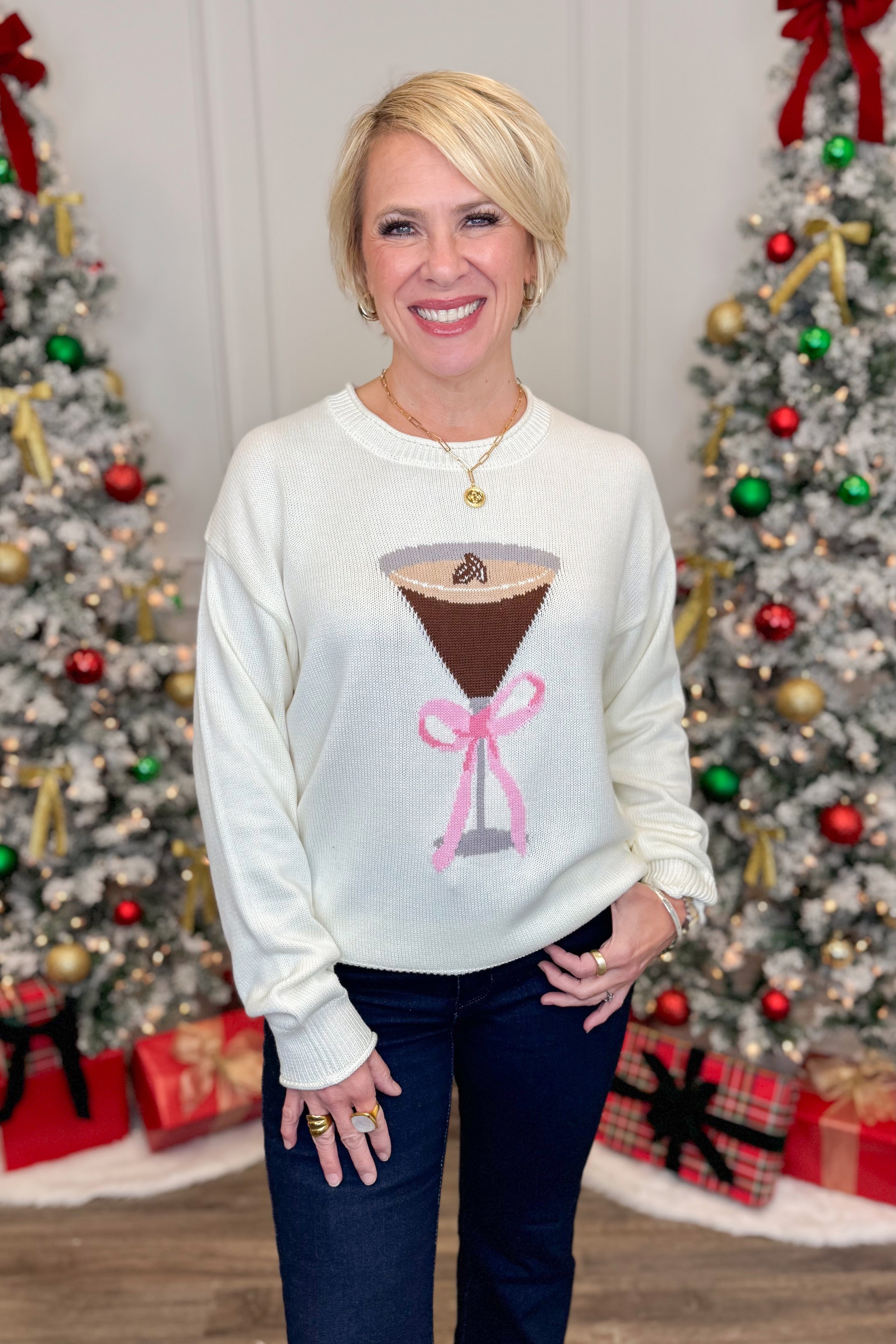 Front view of woman wearing White Espresso Martini With Bow Sweater with jeans in front of holiday decor.