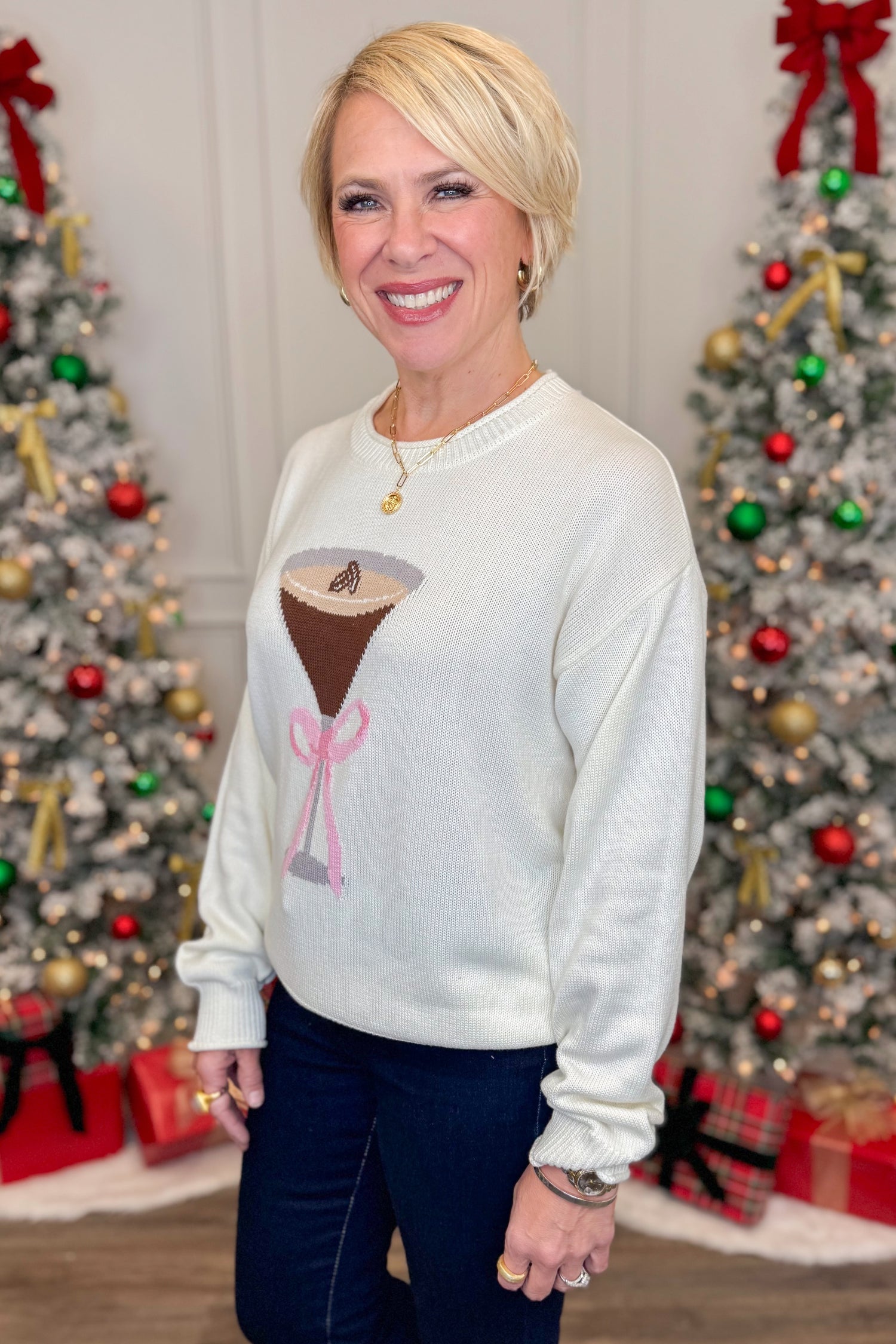 Side view of woman wearing White Espresso Martini With Bow Sweater with jeans in front of holiday decor.