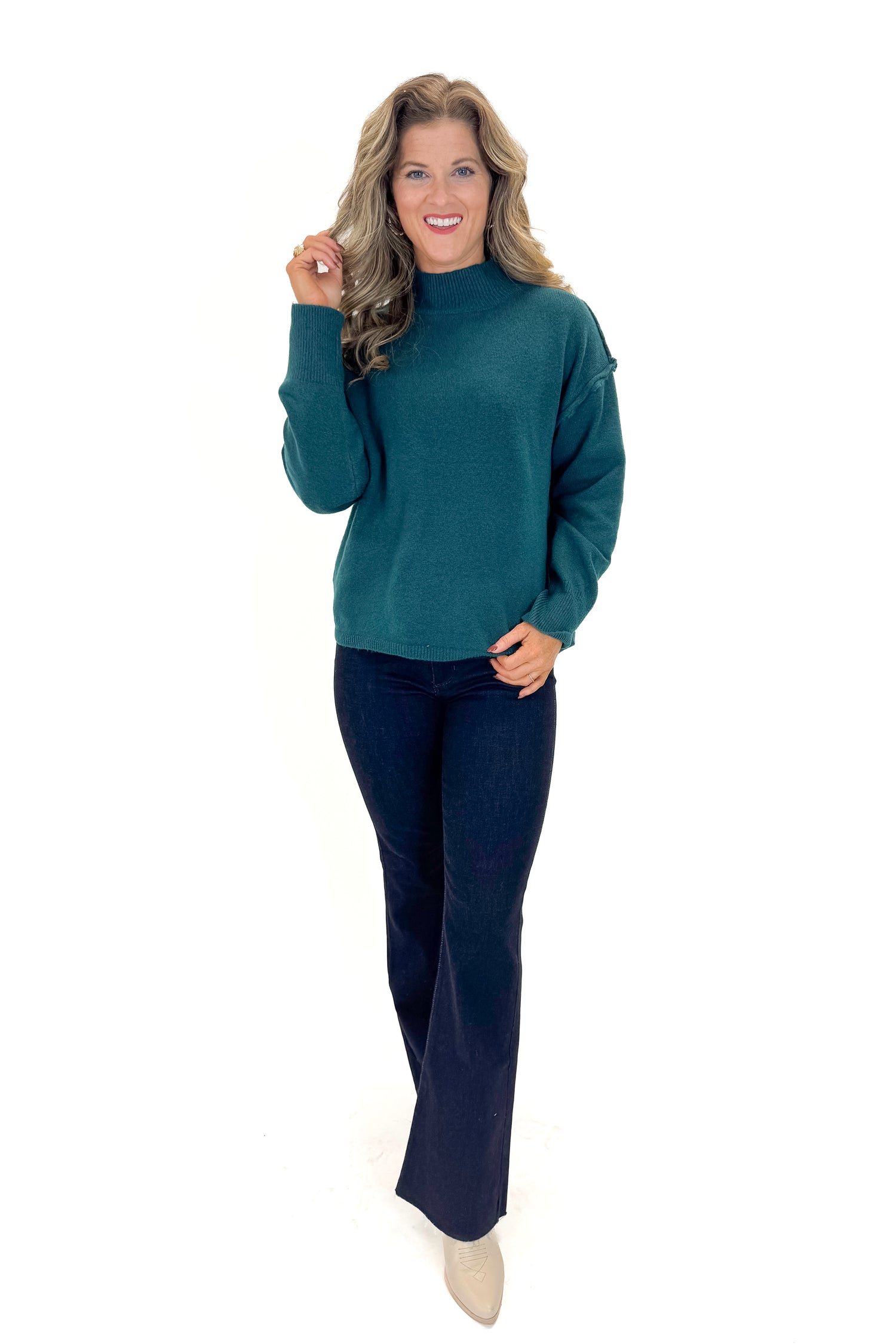 Front view of woman wearing Green Mock Neck Sweater with jeans against white studio background.