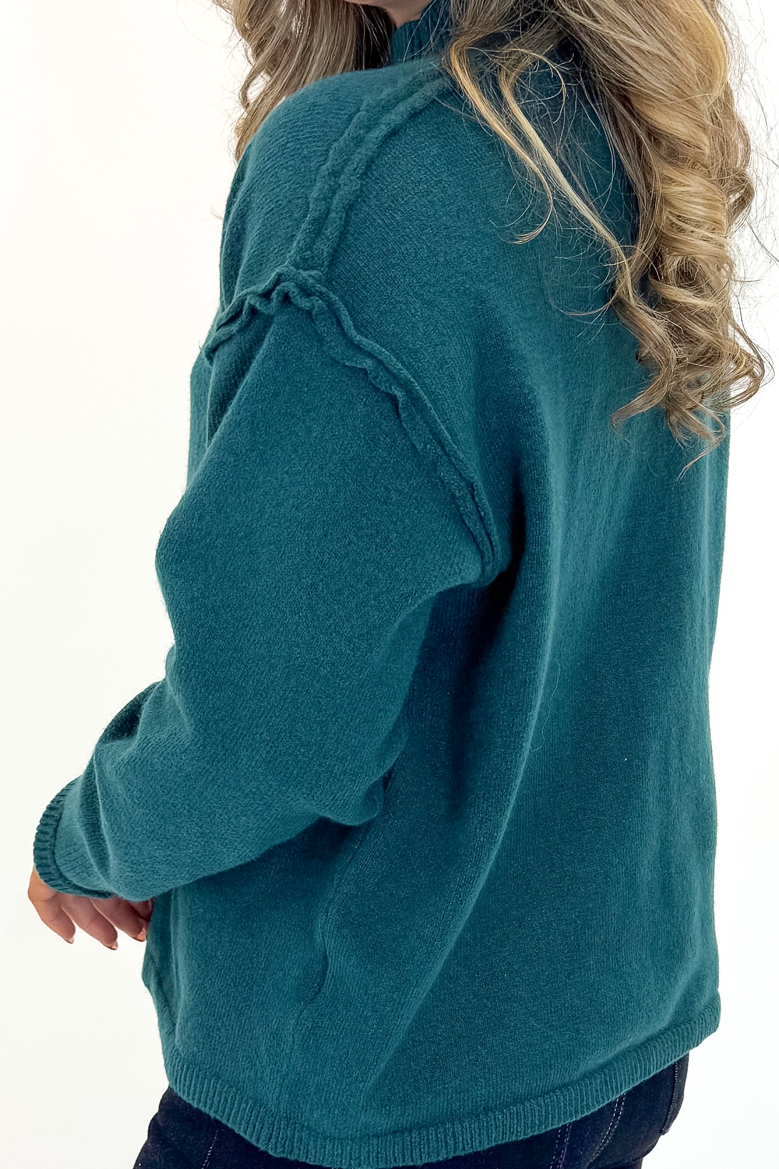 Side detail view of woman wearing Green Mock Neck Sweater with jeans against white studio background.