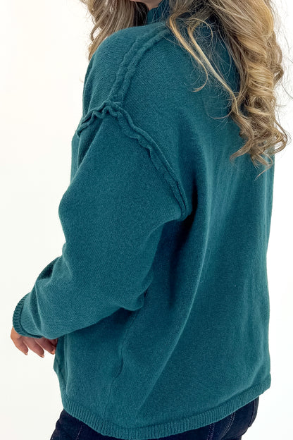 Side detail view of woman wearing Green Mock Neck Sweater with jeans against white studio background.