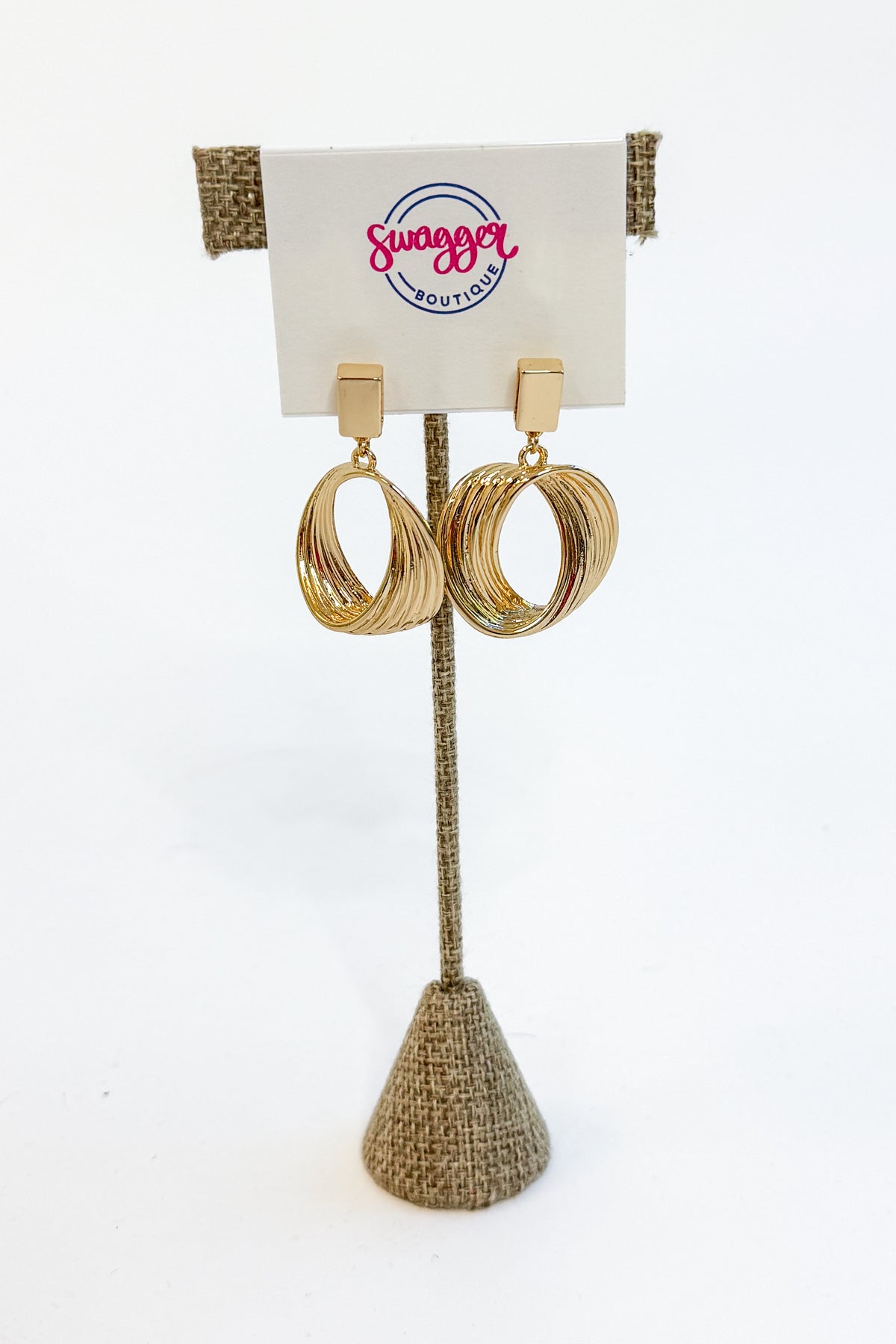 A pair of gold-toned triple-hoop dangle earrings displayed on a burlap-covered stand with a white card labeled &