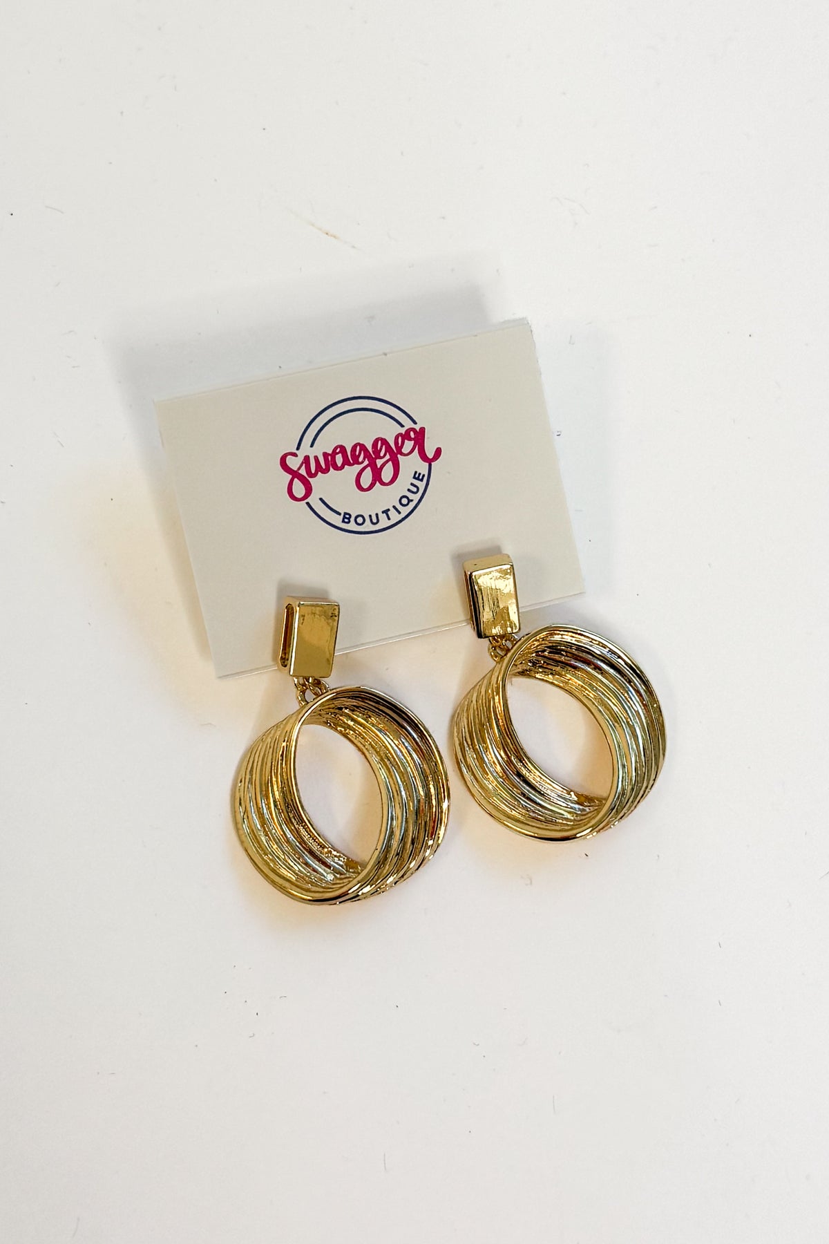 A pair of gold-toned hoop earrings with a twisted, layered design, displayed on a white card labeled &