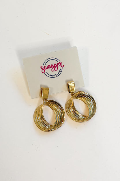 A pair of gold-toned hoop earrings with a twisted, layered design, displayed on a white card labeled &