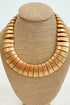 Front view of a chunky gold collar necklace displayed on a beige jewelry bust, featuring layered fan-shaped links.