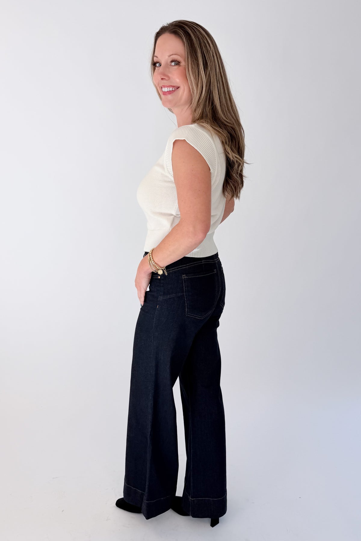 Side view of woman wearing Swagger Boutique’s sweater with Maya Wide Leg Jeans In Dark Wash- Amaze by Kut from the Kloth against white studio background.