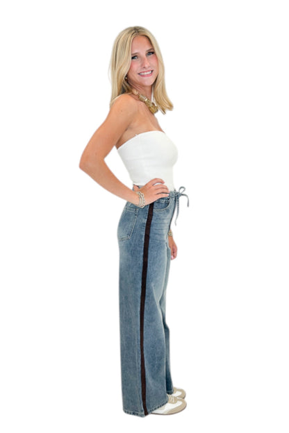 Side view of woman wearing Swagger Boutique’s Medium Wash Brown Stripe Detail Jeans against white studio background.