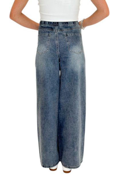 Back view of woman wearing Swagger Boutique’s Medium Wash Brown Stripe Detail Jeans against white studio background.