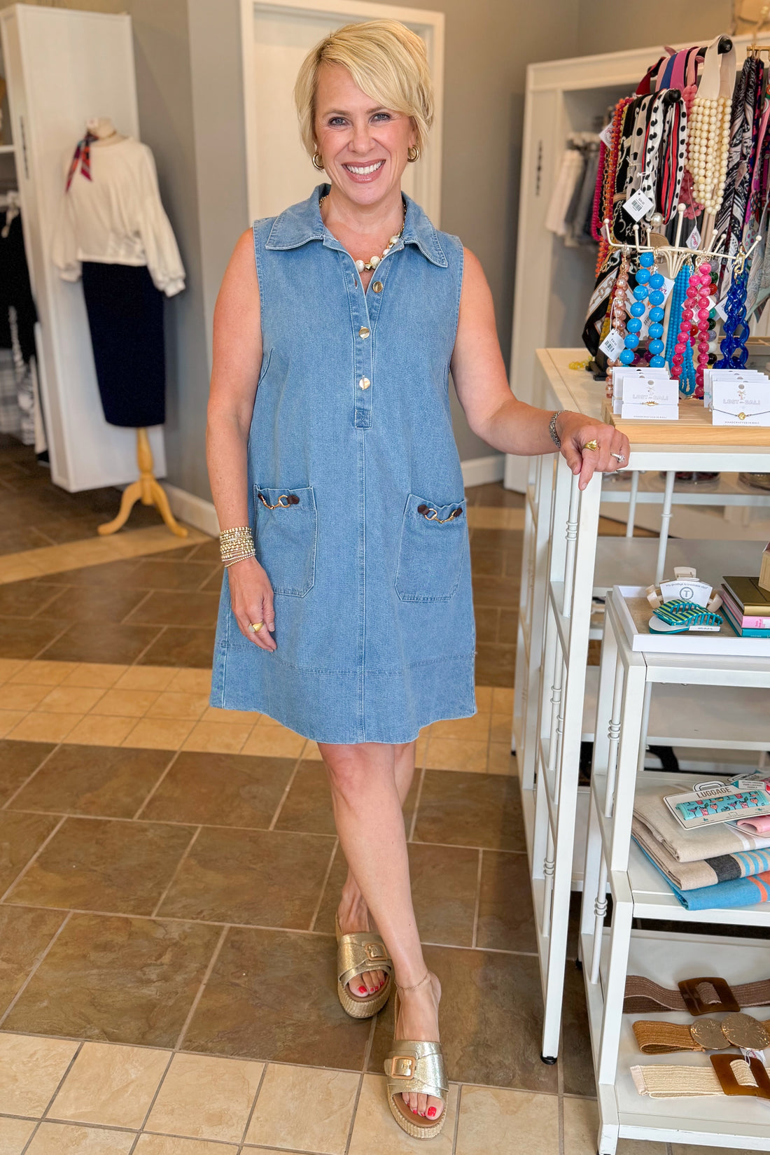 Front view of woman wearing Swagger Boutique’s Medium Wash Sleeveless Denim Midi Dress by Entro with sandals at the store.
