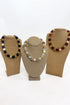 Three chunky beaded necklaces of  alternating polished gold cube beads and stone beads, displayed on tan burlap-covered jewelry busts against a white background.