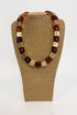 Chunky statement necklace with alternating translucent amber-brown beads and square gold-tone metal cubes, displayed on a tan fabric jewelry bust against a white background.