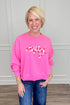 A smiling blonde woman wearing a bright pink crewneck sweatshirt with &