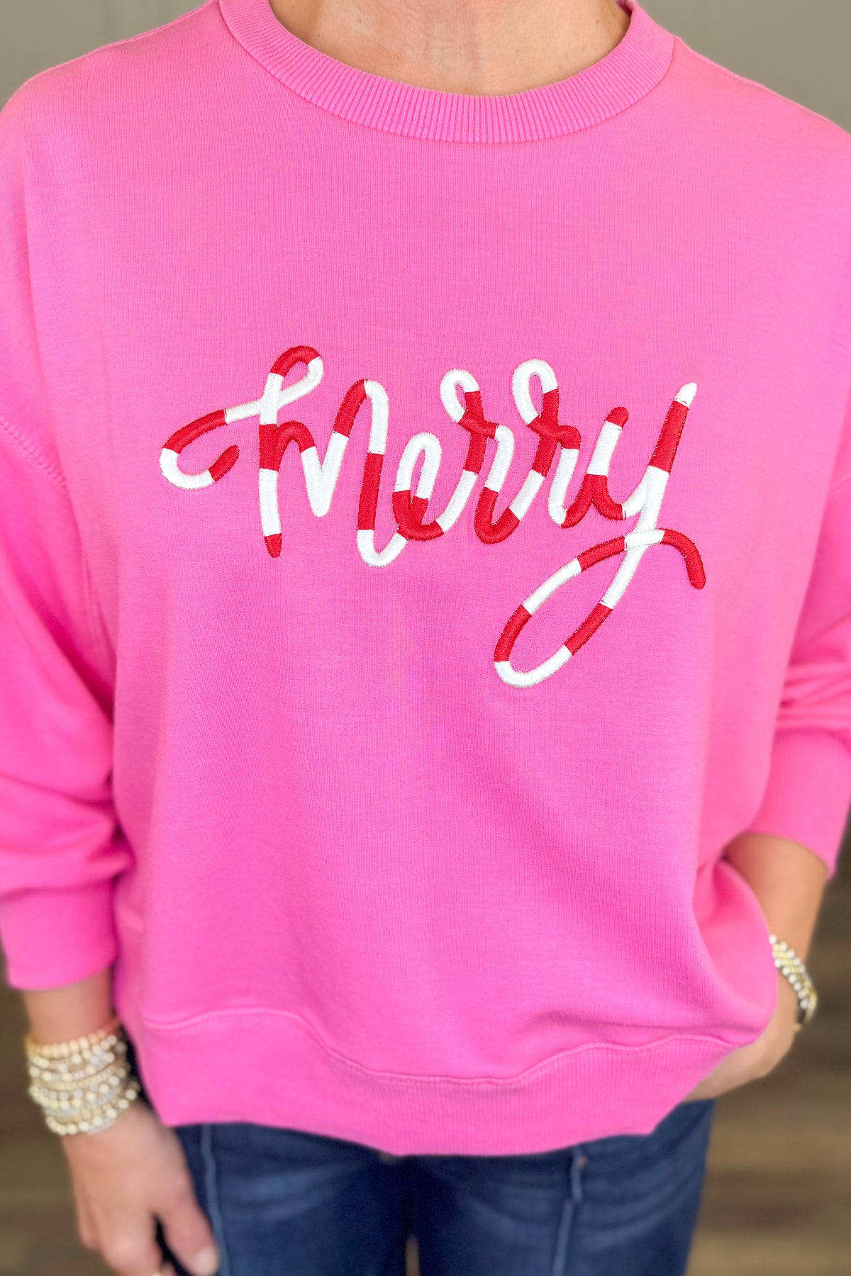 A close-up of a person wearing a bright pink crewneck sweatshirt with the word &