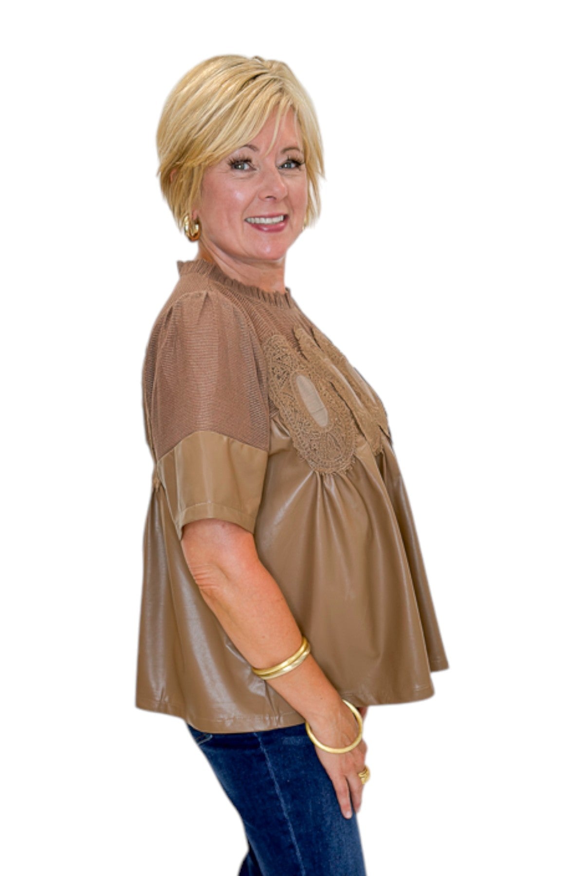 Side view of woman wearing Swagger Boutique’s Mocha Lace Applique Faux Leather Top with jeans against white studio background.