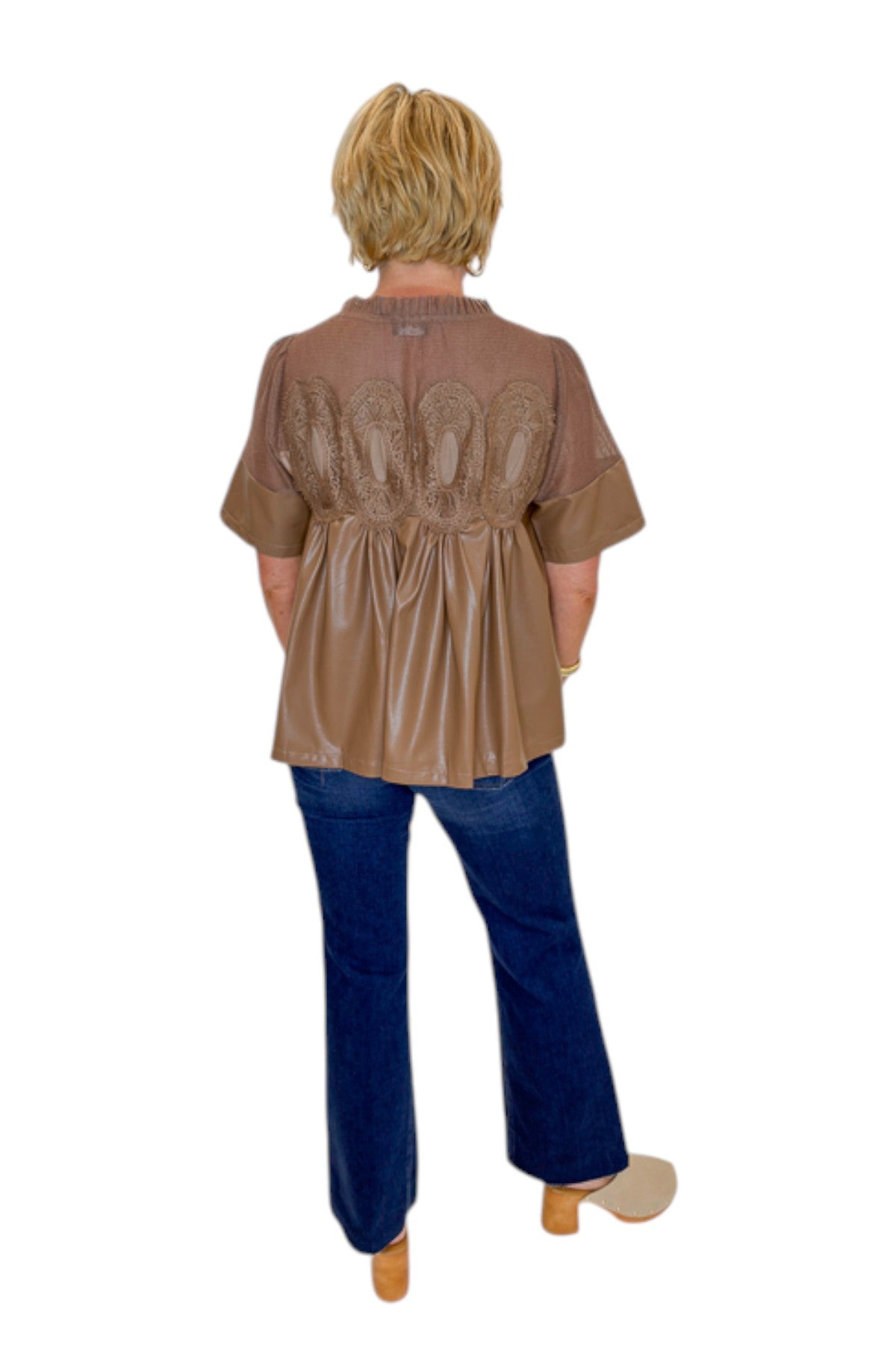 Back view of woman wearing Swagger Boutique’s Mocha Lace Applique Faux Leather Top with jeans against white studio background.