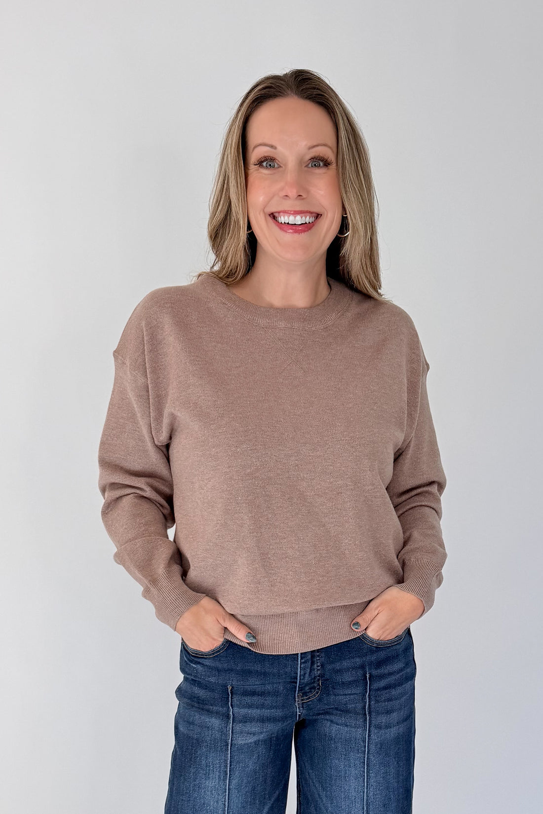 Front view of woman wearing Swagger Boutique’s Mocha Ribbed Hem Sweatshirt with jeans against white studio background.