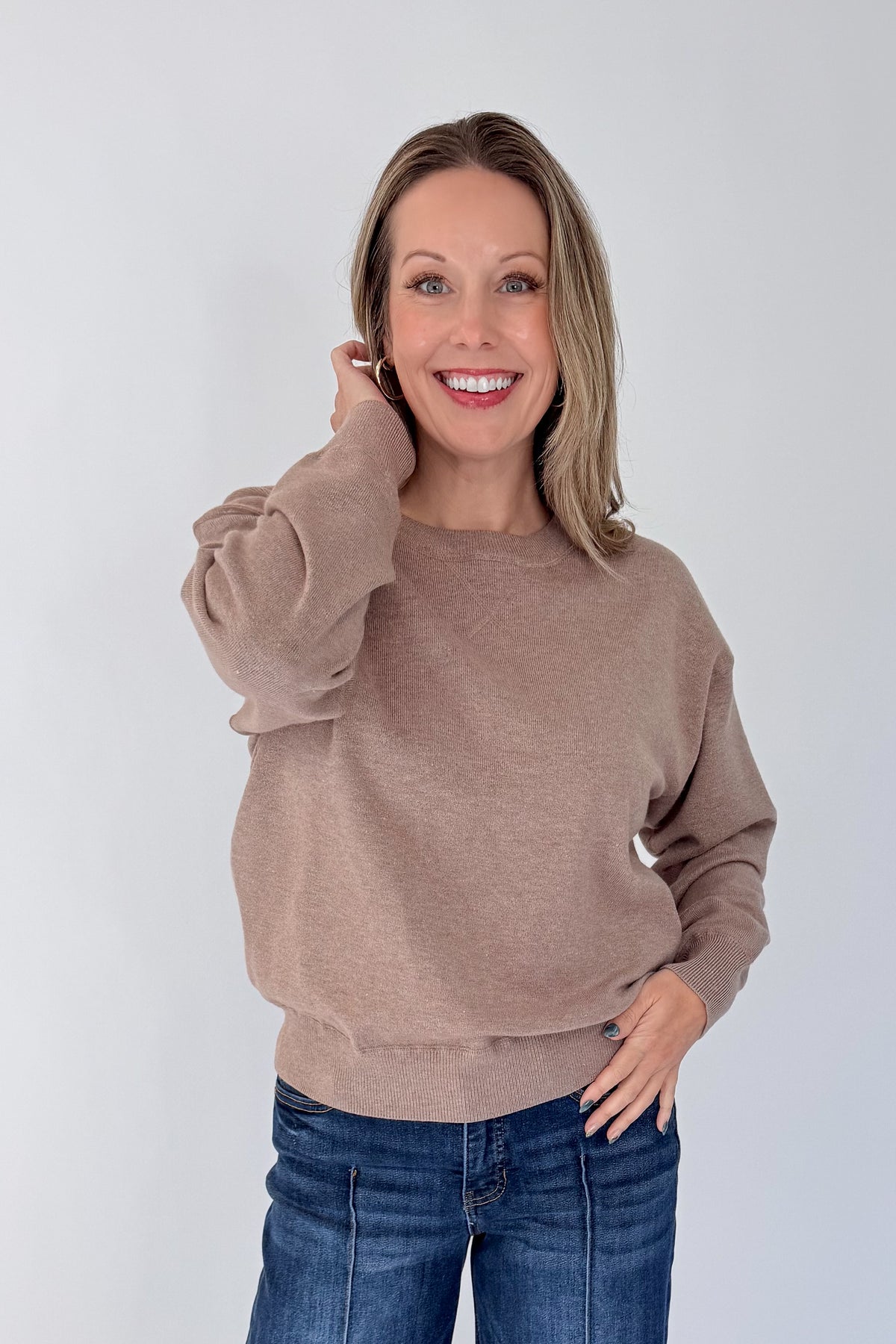Front view of woman wearing Swagger Boutique’s Mocha Ribbed Hem Sweatshirt with jeans against white studio background.