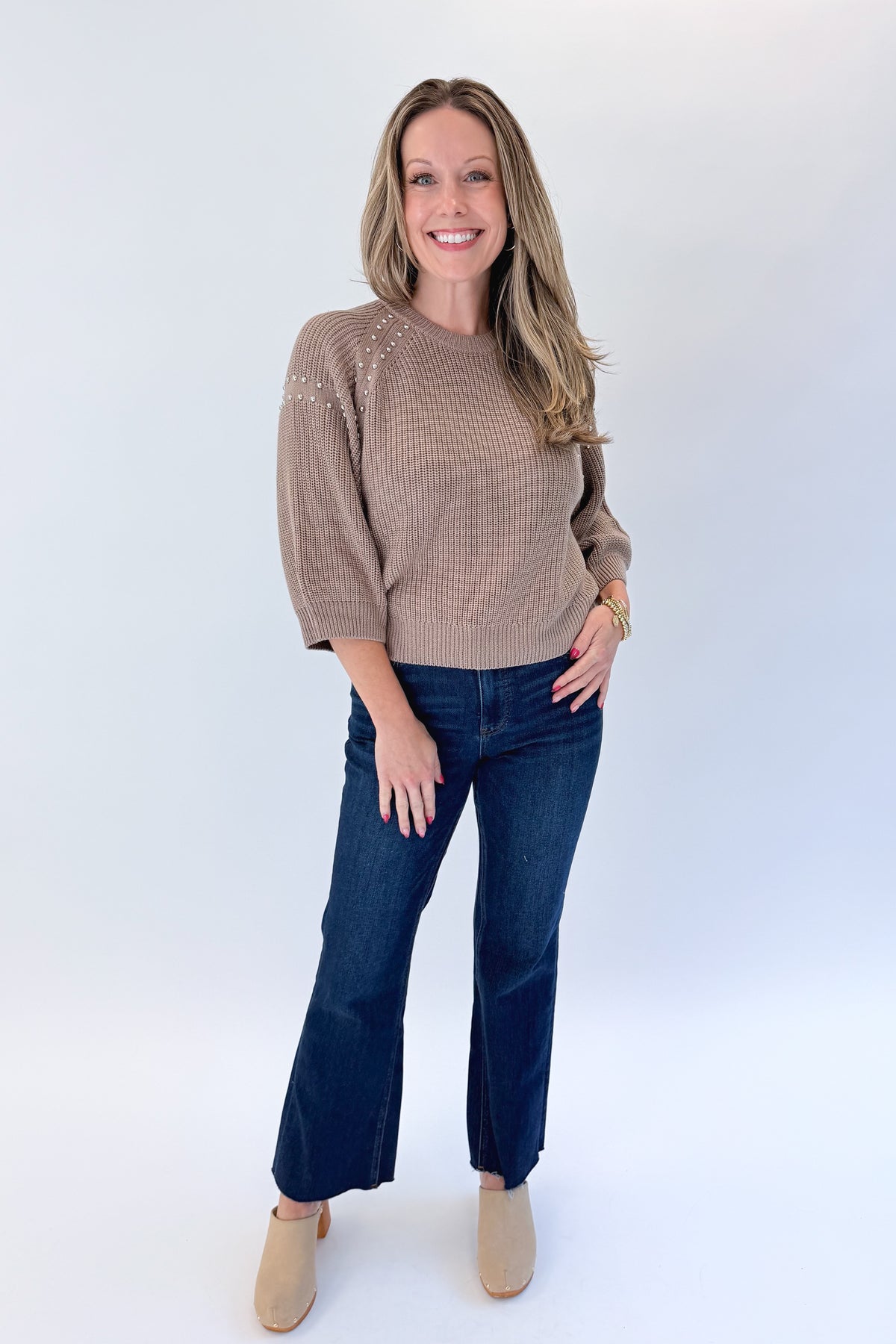 Front view of woman wearing Swagger Boutique’s Mocha Stud Detail Sweater by Entro with jeans against white studio background.