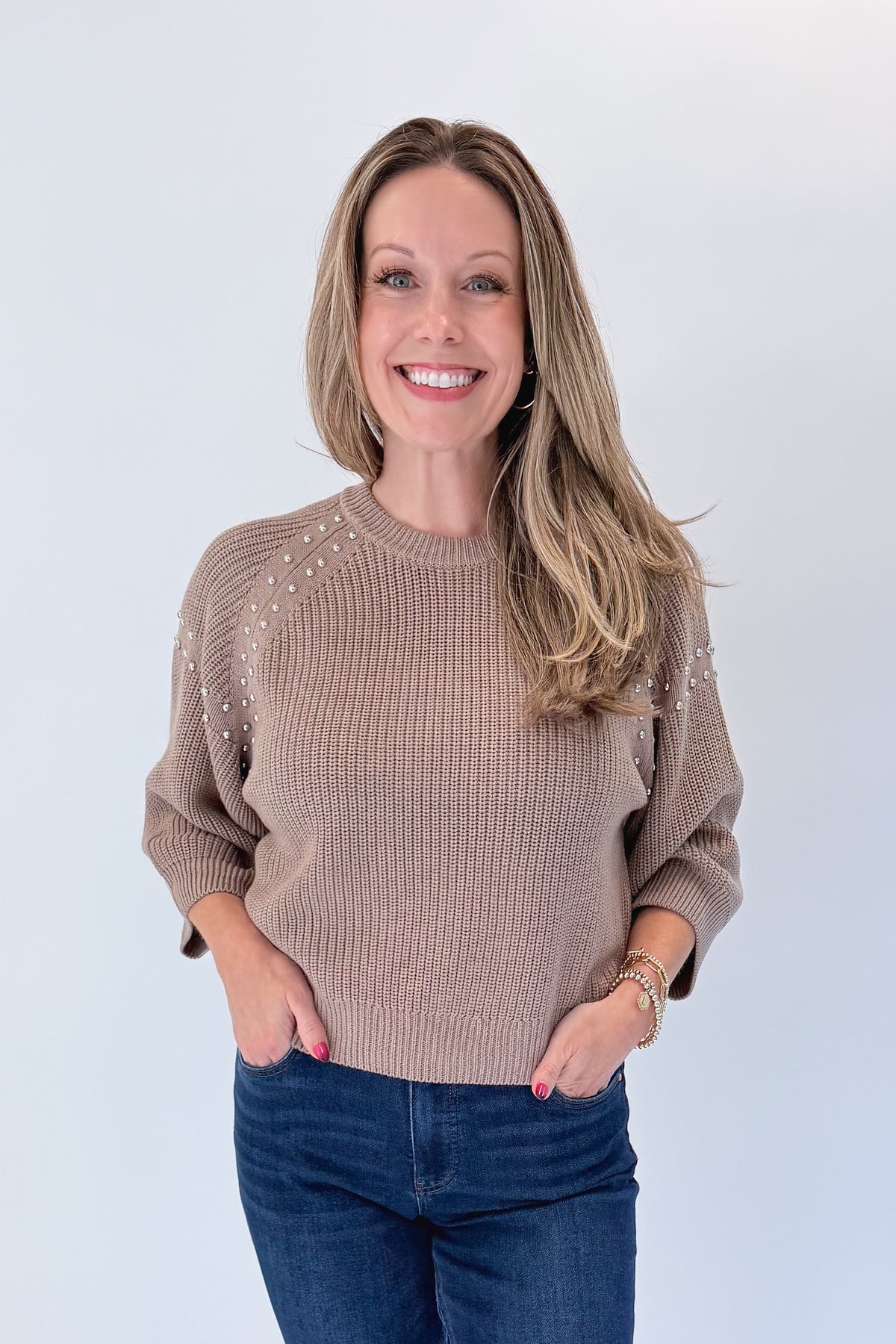 Front view of woman wearing Swagger Boutique’s Mocha Stud Detail Sweater by Entro with jeans against white studio background.