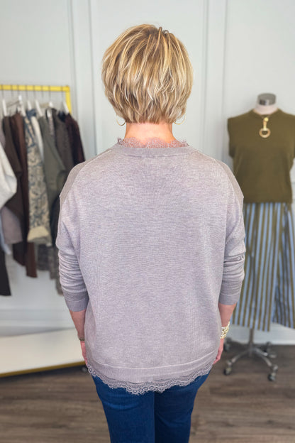 Back view of woman wearing Swagger Boutique’s Mocha Lace Lined V-Neck Sweater  with jeans with clothing hanging in the background.