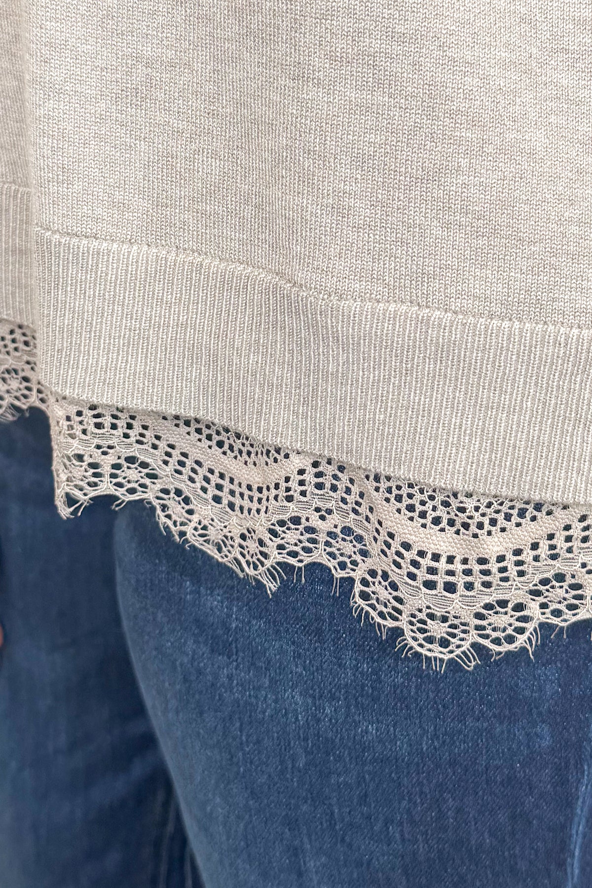 Front detail view of woman wearing Swagger Boutique’s Mocha Lace Lined V-Neck Sweater  with jeans with clothing hanging in the background.