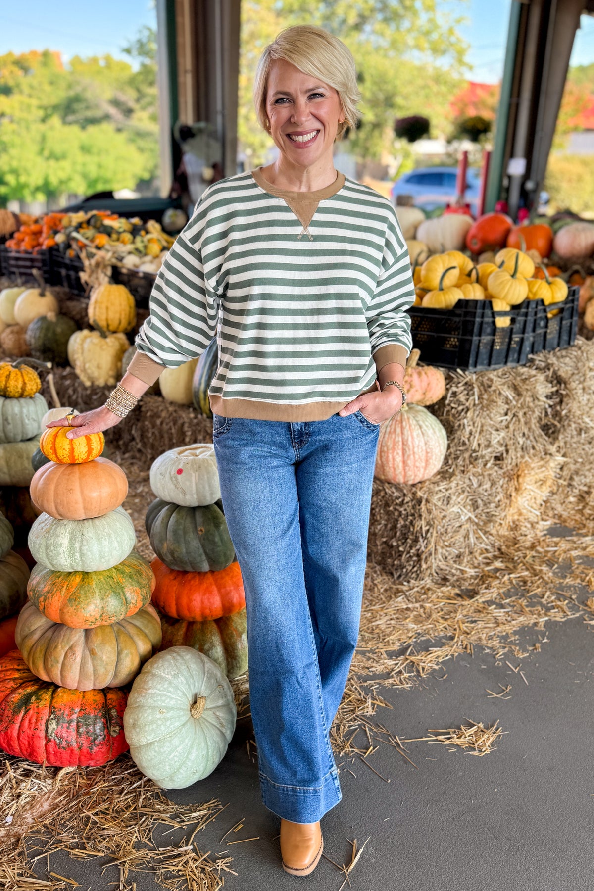 Front view of woman wearing Swagger Boutique’s Monstera Low Key Stripe Sweatshirt by Z Supply with jeans standing at a pumpkin patch.
