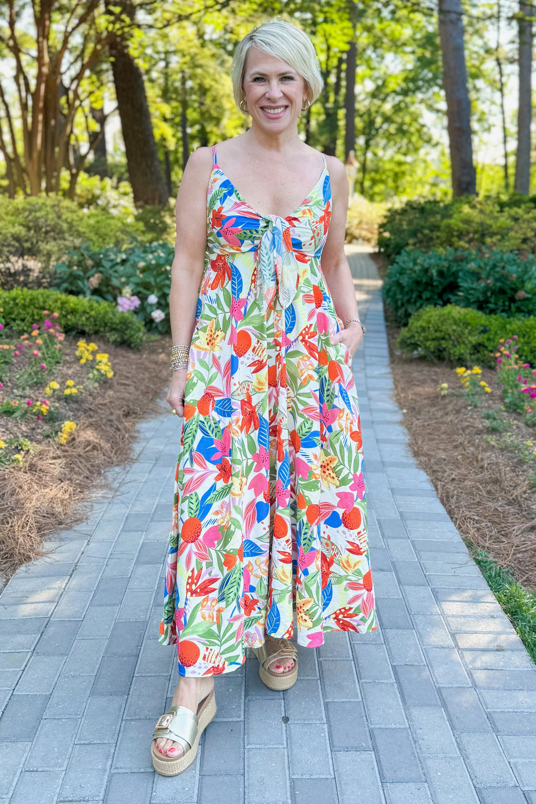 Front view of woman wearing Swagger Boutique’s Multi Floral Midi Dress walking outside on a path.