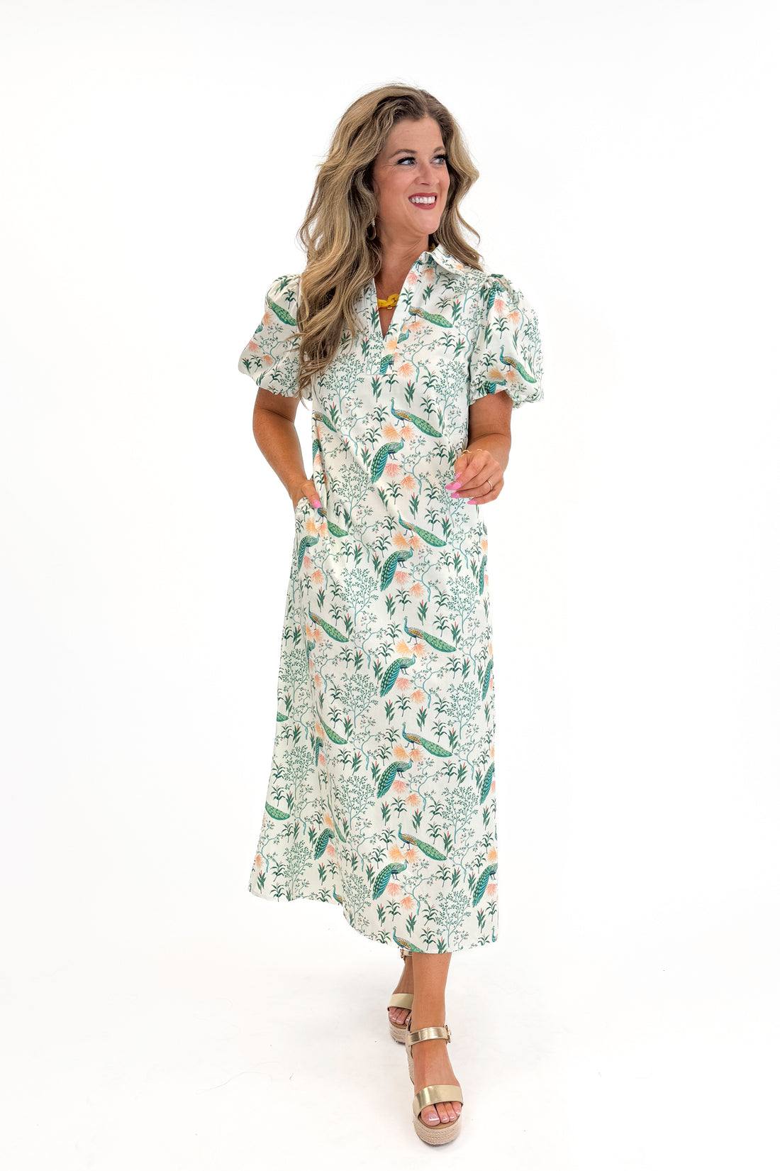 Front view of woman wearing Swagger Boutique’s Multi Peacock Print Maxi Dress with sandals against white studio background.