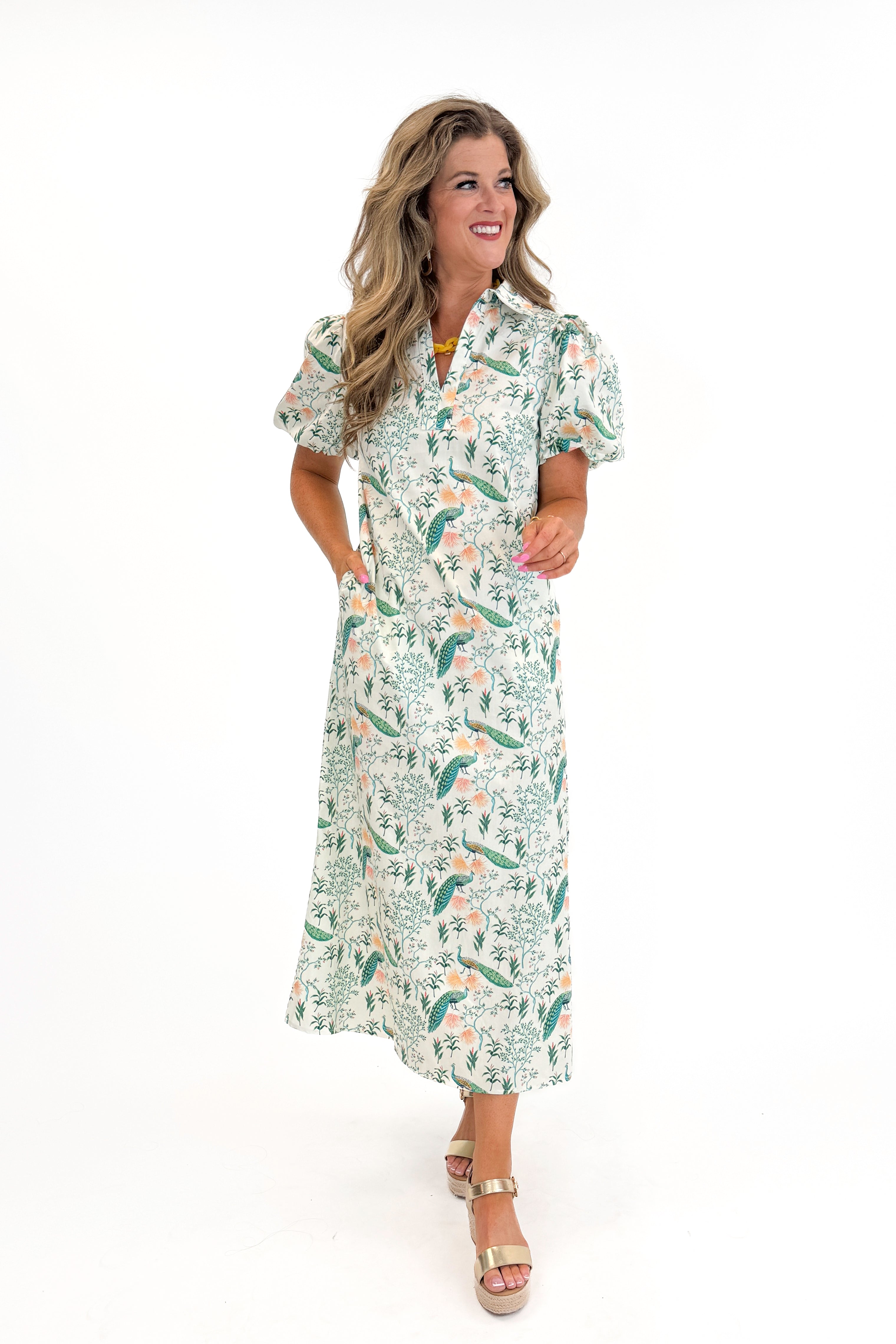 Front view of woman wearing Swagger Boutique’s Multi Peacock Print Maxi Dress with sandals against white studio background.