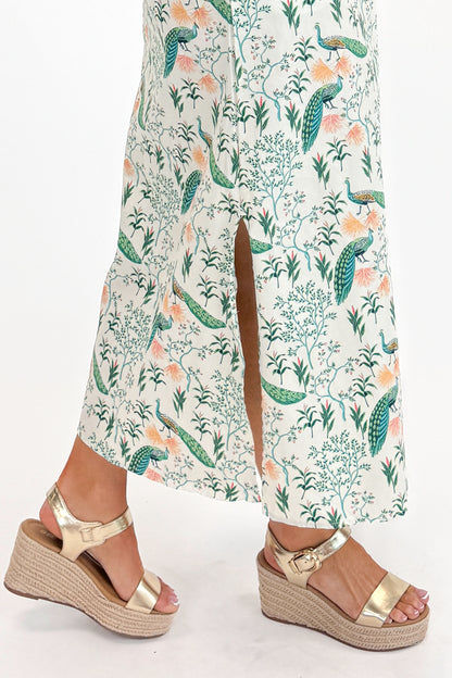 Side detail view of woman wearing Swagger Boutique’s Multi Peacock Print Maxi Dress with sandals against white studio background.