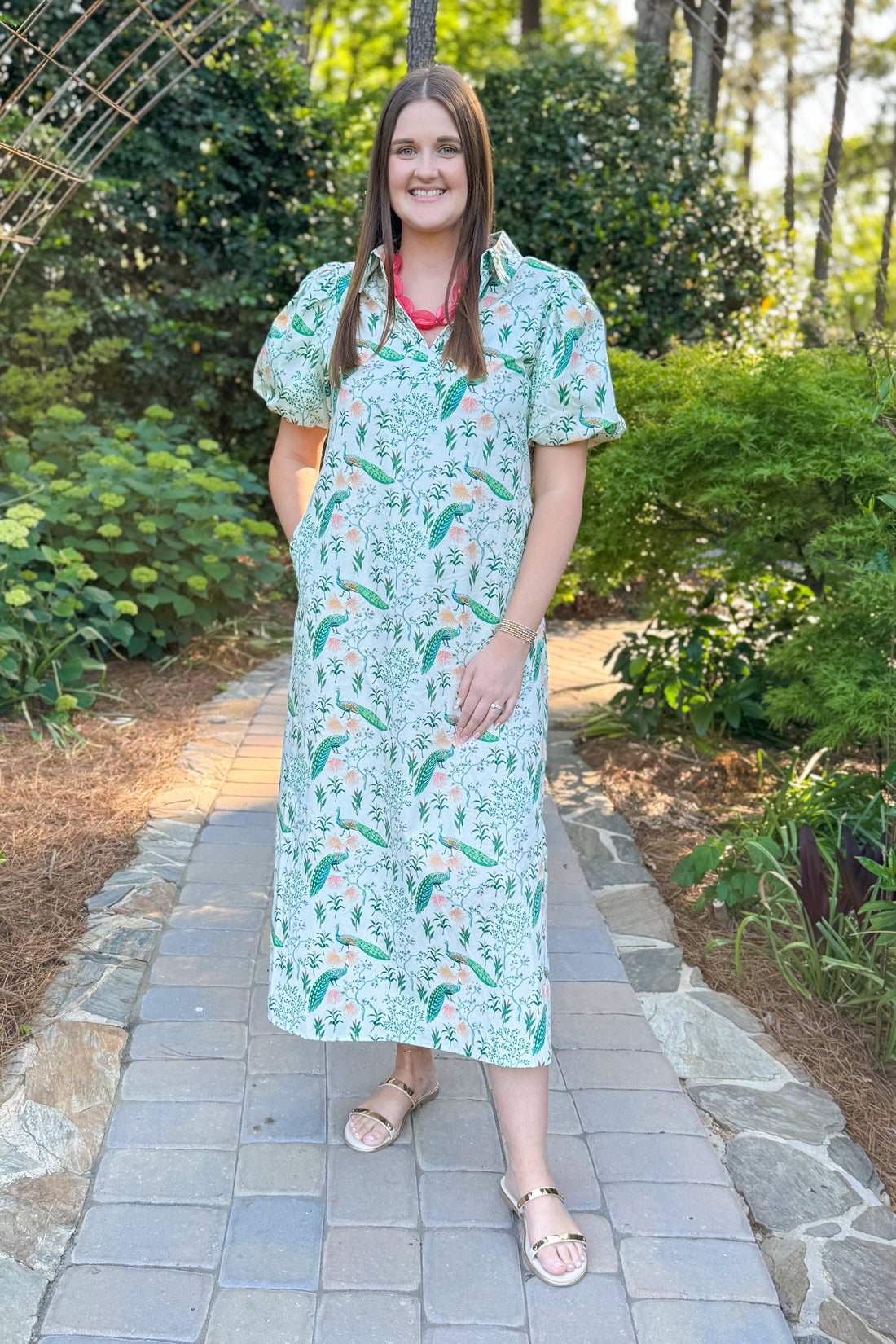 Front view of woman wearing Swagger Boutique’s Multi Peacock Print Maxi Dress with sandals standing outside on a path.