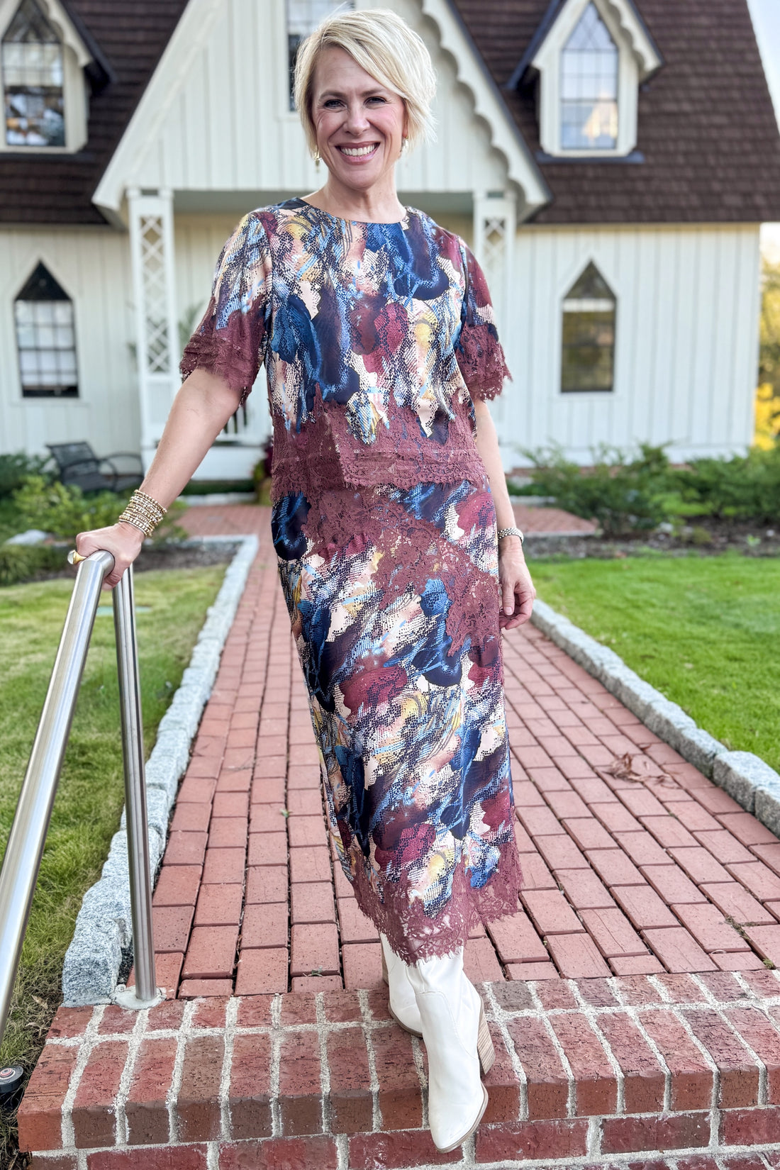Front view of woman wearing Swagger Boutique’s Multi Snake Print Lace Trim Top with Multi Snake Print Lace Trim Midi Skirt standing in front of a white house.