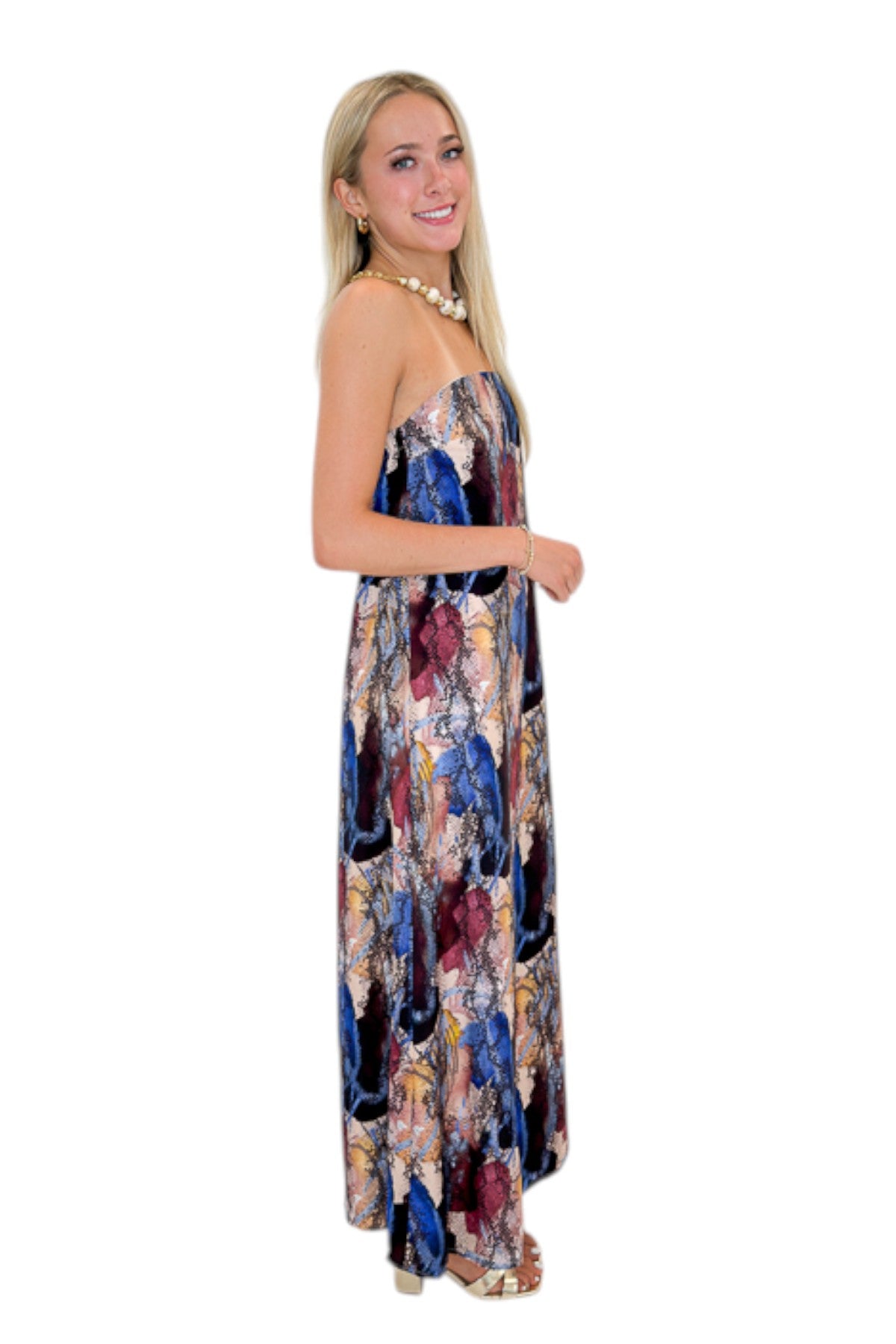 Side view of woman wearing Swagger Boutique’s Multi Snake Print Strapless Maxi Dress with heels against white studio background.